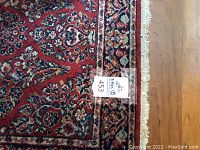 Close-up of burgundy floral rug edge and fringe showing detailed pattern and colors.