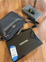 Photo showing Toshiba laptop, black laptop carrying case, and Ruger lockable case on floor