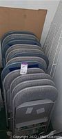 Stack of grey and blue folding chairs showing the tops of backs and some seats.