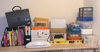 Wide view showing various office supplies on table including laminator, storage bins, binders, file folders, level tool, and boxes.