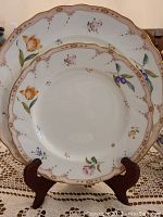 Photo showing Noritake Maison Fleur dinner plates with floral patterns and gold trim displayed on stands.