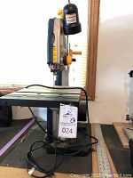 Side view of Ryobi band saw on its stand with power cord and 36-inch metal ruler beside it.
