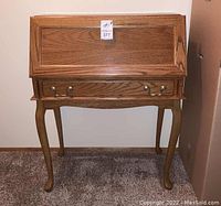 Front view of oak secretary desk with closed fold-down panel and two metal drawer pulls on bottom drawer.
