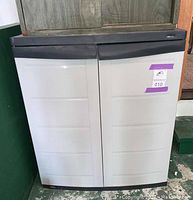 Front view of beige plastic storage cabinet with two doors and black top.