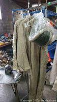 Two beige Arcguard Protective Arc 40 jackets and overalls with a face shield hanging on a rack
