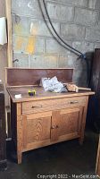 Wood cabinet with backsplash against a concrete wall; visible scratches and nicks on surface; brass handle on drawer and wooden knobs on doors