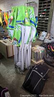 Folded canopy frame with green fabric top standing in warehouse, black carrying bag on floor.