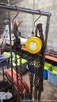 Yellow metal 2 ton chain hoist hanging on metal rack with chained link and large hook, showing surface rust in a workshop setting.