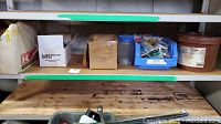 Shelf showing multiple cardboard boxes containing a variety of hardware items including chains, locks, keys, and other components.