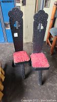 Front view of two vintage tripod chairs with tall dark wooden backrests and red seat cushions on a concrete floor.