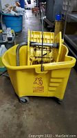 Yellow industrial mop bucket with metal wringer on top.