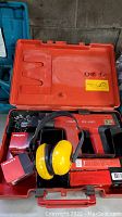 Open orange carrying case showing Hilti DX 450 nail gun, yellow earmuffs, and cartridge boxes
