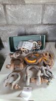 Photo of multiple rusted iron anchor shackles, a large yellow industrial hook, and green metal tin with chains on a white surface against a gray wall.
