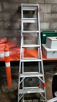 Front view of folded aluminum ladder standing upright showing multiple steps and sections.