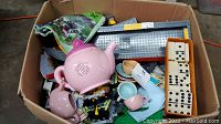 Box showing pink toy tea set, Lego baseplates, and pieces with partial view of dominoes