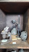 Open wooden box containing Swift Stereo Ninety microscope and separate magnifying lamp with metallic shade mounted on board