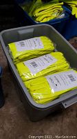 Plastic bin filled with multiple packs of yellow Chem Brite safety gloves packed in clear plastic, stacked neatly.