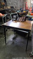 Full view of the square sewing table with metal legs and worn wooden top.