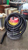 Front view of Interclean shop vacuum showing red top, yellow power cord coiled around top, and black coiled hose attached.