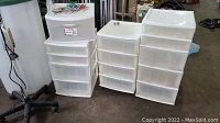 Four white plastic storage drawer sets grouped together, including one on casters.