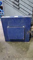 Full view of the closed blue wooden key box showing front square pocket and door hinges.