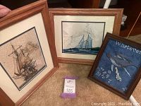 Photo shows three framed art pieces on carpet. Two larger are nautical chart prints of sailing ships in wooden frames. Third smaller framed art shows whales and clock numbers on dark blue background.