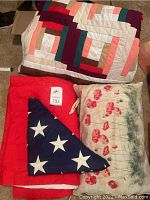 Photo showing folded American flag placed on red quilt and floral pillow alongside multi-colored quilt with geometric patterns