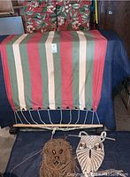 Large striped hammock with green, red, cream, and tan vertical stripes, shown folded with visible rope attachments at bottom.
