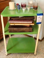 Side and partial top view of green metal cart with items on shelves including photo albums and candles