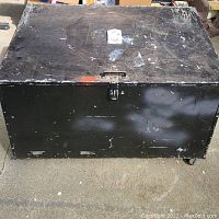 Photo of the top and front view of the metal trunk showing the latch, paint wear, and wheels.