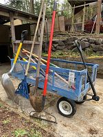 Photo of blue metal utility cart loaded with outdoor garden tools leaning against the side.
