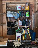 Overview of wooden shelving unit filled with multiple garden and garage items including boots, folded tarps, containers, loppers, and small tools.