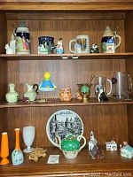 Full view of three shelves filled with pottery, ceramic figurines, glass beer mugs, vases, and various decorative items.