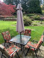 Full patio set with table, umbrella, granite base, and four cushioned folding chairs arranged outside on concrete patio.