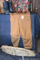 Camel colored Walls coveralls size 2XL, black Servus rubber boots size 13, and khaki Allen hunting case displayed on a blue padded surface.