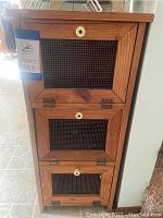 Front view of wooden potato holder cabinet with three wire mesh pull-out drawers and white round knobs.