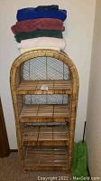 Front view of round top wicker shelving unit with four slatted shelves and stacked towels on top in various colors.