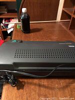 Black Royal Duper Guard laminating machine with power cord on wooden desk surface.