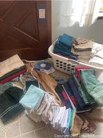 Laundry basket filled with folded linens including towels and clothing items stacked next to it on floor.