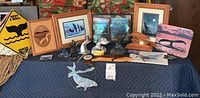 Wide view showing full lot of whale decor items on a blue quilted blanket including plaques, prints, sculptures, and magnets.