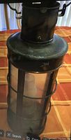 Close-up photo of a vintage metal lantern with glass panel, showing patina and wear.