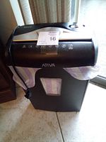Ativa black document shredder standing on floor with visible control panel, shred slot, power cord, and transparent window for shredded material.