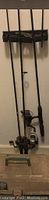 Three fishing rods standing upright in a rod holder against the wall, showing handles and reels.