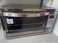 Front view showing the large glass door, digital control panel, and interior rack of the stainless steel convection oven.