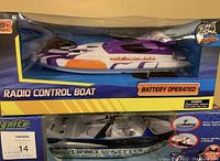 Photo showing the purple and white radio control boat in unopened box with 'Battery Operated' and '2.4 GHz' control frequency labels.