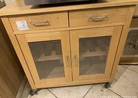 Front view of the wooden kitchen cart showing two metal handle drawers, two mesh panel cabinet doors, and caster wheels at the base.