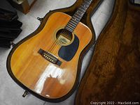 Full view of acoustic guitar inside open hard shell case, showing top, pickguard, and bridge.