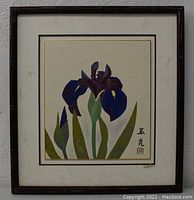 Full view of the original painting showing purple iris flowers in a dark brown frame with matting on a white wall.