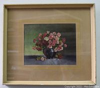 Framed floral print showing a bouquet of multicolored roses in a blue-black vase with petals on a surface, captured from a slight angle revealing the frame condition.
