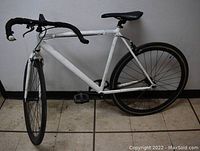 Left side view of the white road bicycle showing the full frame, rear wheel, pedals, seat post, and chain setup.